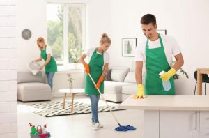 Three individuals in green aprons are cleaning a room for a home cleaning service.