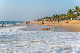 Tourists enjoying a peaceful beach in Kerala with gentle sea waves, golden sand, coconut trees, and clear blue skies along the Arabian Sea coastline.