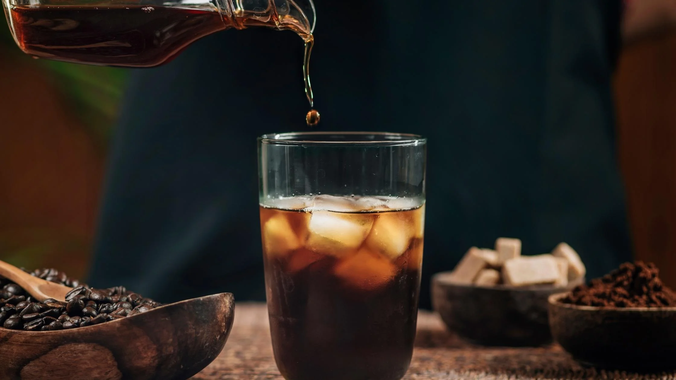 Refreshing cold brew poured over ice beside coffee beans, representing iced americano and chilled black coffee recipes.