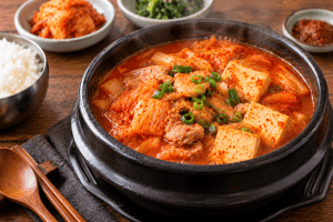 Traditional Korean food featuring spicy kimchi jjigae stew with tofu, cabbage, meat, and green onions.